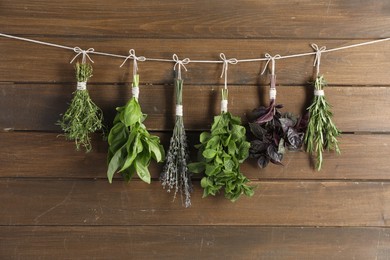 Photo of Bunches of different aromatic herbs hanging on rope near wooden wall