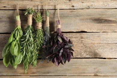 Bunches of different aromatic herbs hanging on rope near wooden wall, space for text