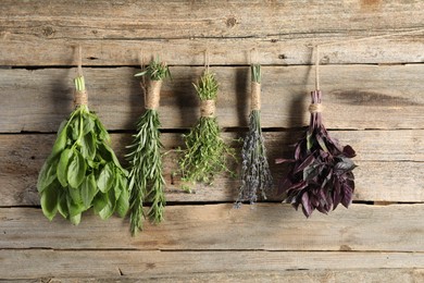 Photo of Bunches of different aromatic herbs hanging on rope near wooden wall