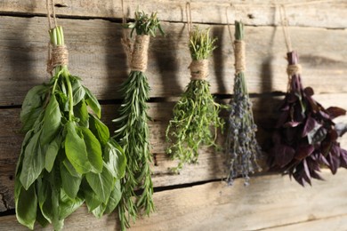 Photo of Bunches of different aromatic herbs hanging on rope near wooden wall, closeup