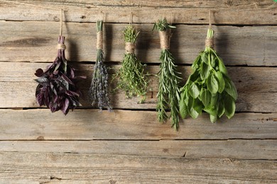 Bunches of different aromatic herbs hanging on rope near wooden wall, space for text