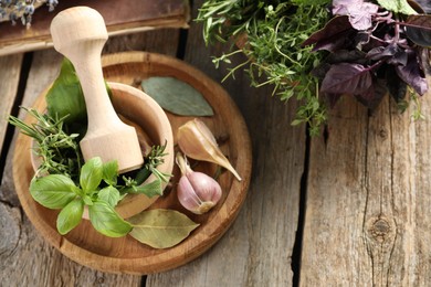 Different aromatic herbs, mortar with pestle and spices on wooden table, flat lay