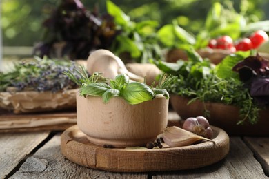 Different aromatic herbs, mortar with pestle and spices on wooden table, closeup