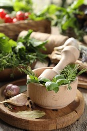 Different aromatic herbs, mortar with pestle and spices on wooden table, closeup