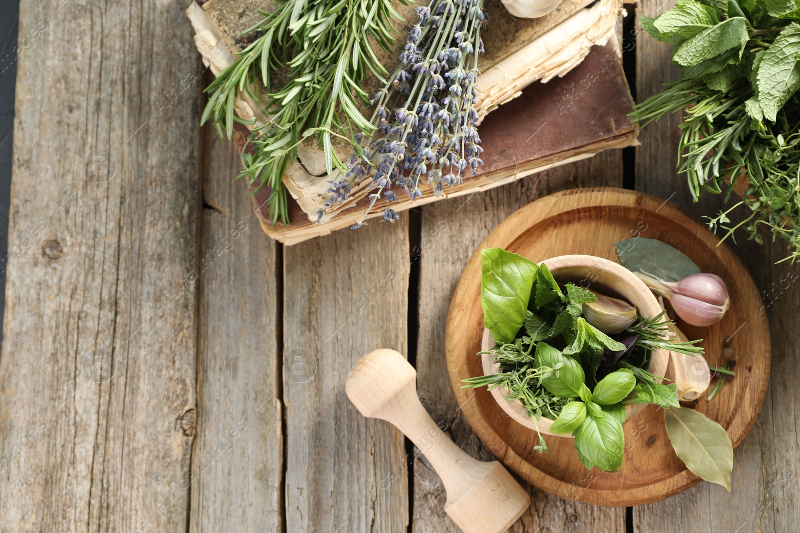 Photo of Different aromatic herbs, mortar with pestle, old books and spices on wooden table, flat lay. Space for text