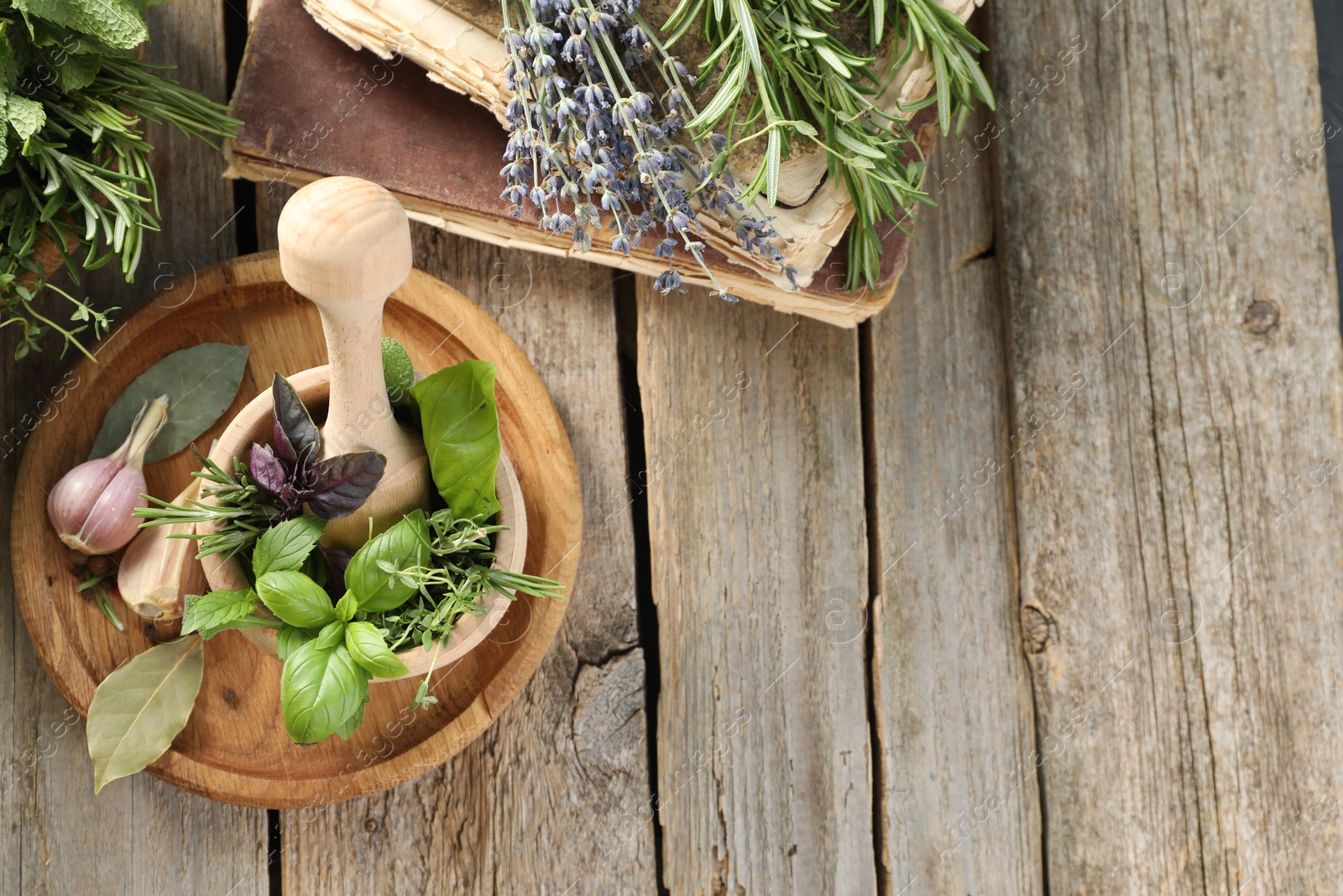 Photo of Different aromatic herbs, mortar with pestle, old books and spices on wooden table, flat lay. Space for text