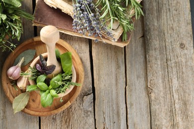 Different aromatic herbs, mortar with pestle, old books and spices on wooden table, flat lay. Space for text