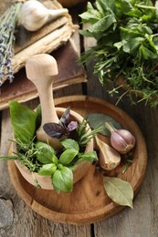 Different aromatic herbs, mortar with pestle, old books and spices on wooden table, above view