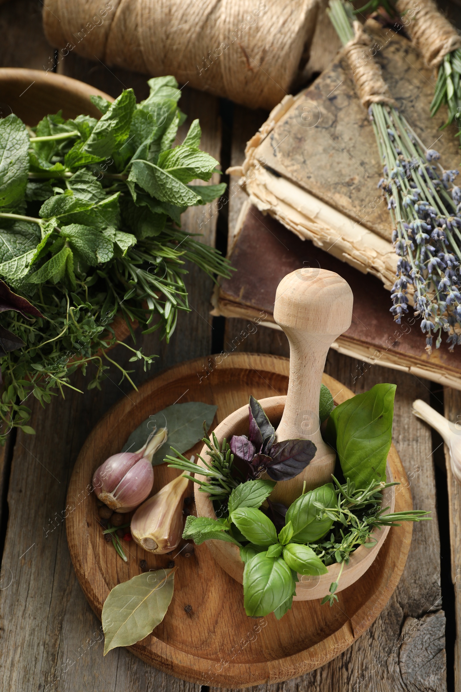 Photo of Different aromatic herbs, mortar with pestle, old books and spices on wooden table, flat lay