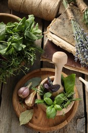 Different aromatic herbs, mortar with pestle, old books and spices on wooden table, flat lay