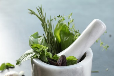 Different aromatic herbs, mortar with pestle on gray background, closeup