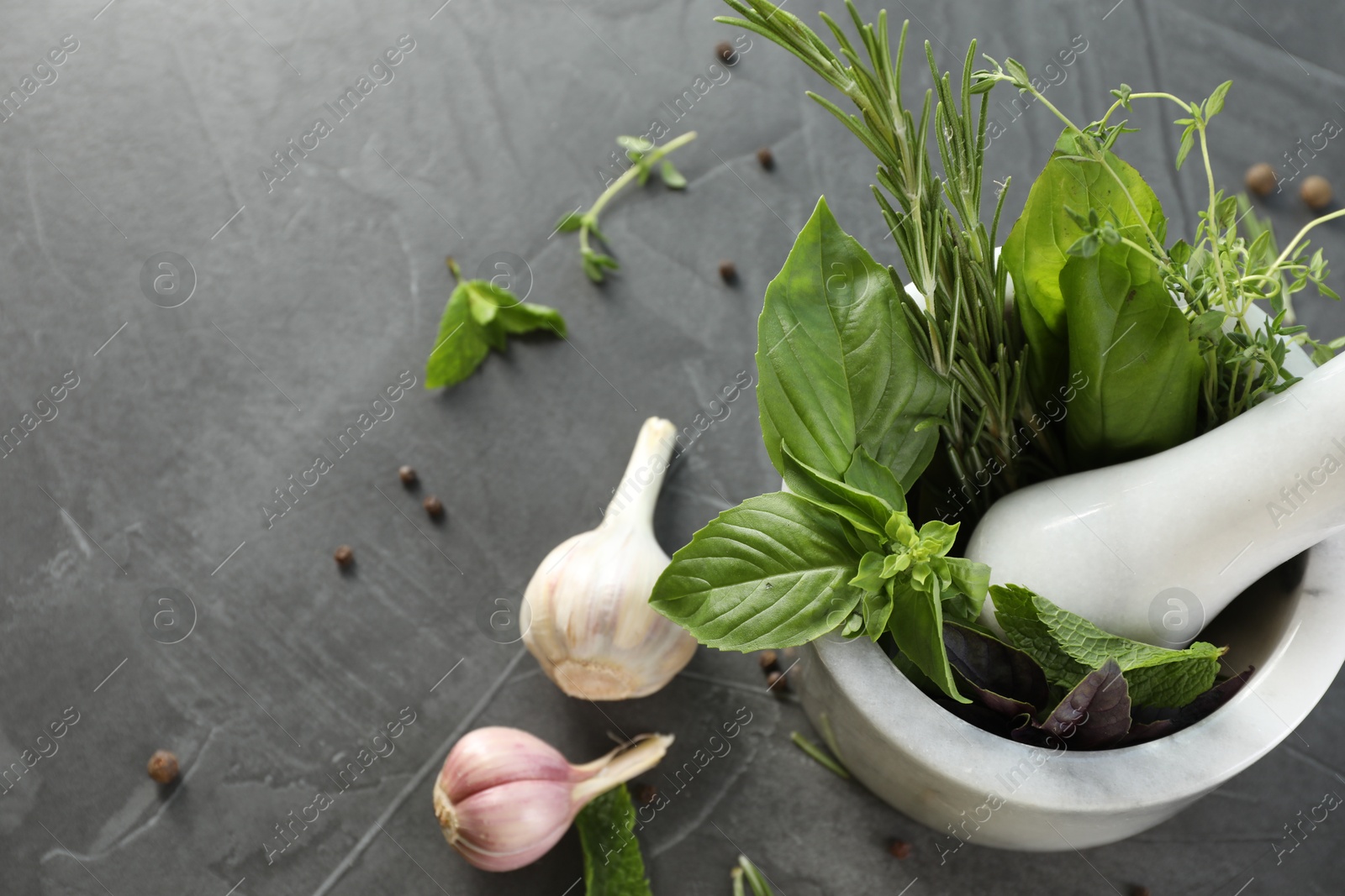 Photo of Different aromatic herbs, mortar with pestle and spices on gray textured table, flat lay. Space for text