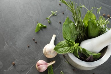 Different aromatic herbs, mortar with pestle and spices on gray textured table, flat lay. Space for text