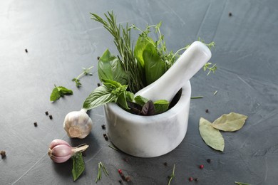 Different aromatic herbs, mortar with pestle and spices on gray textured table