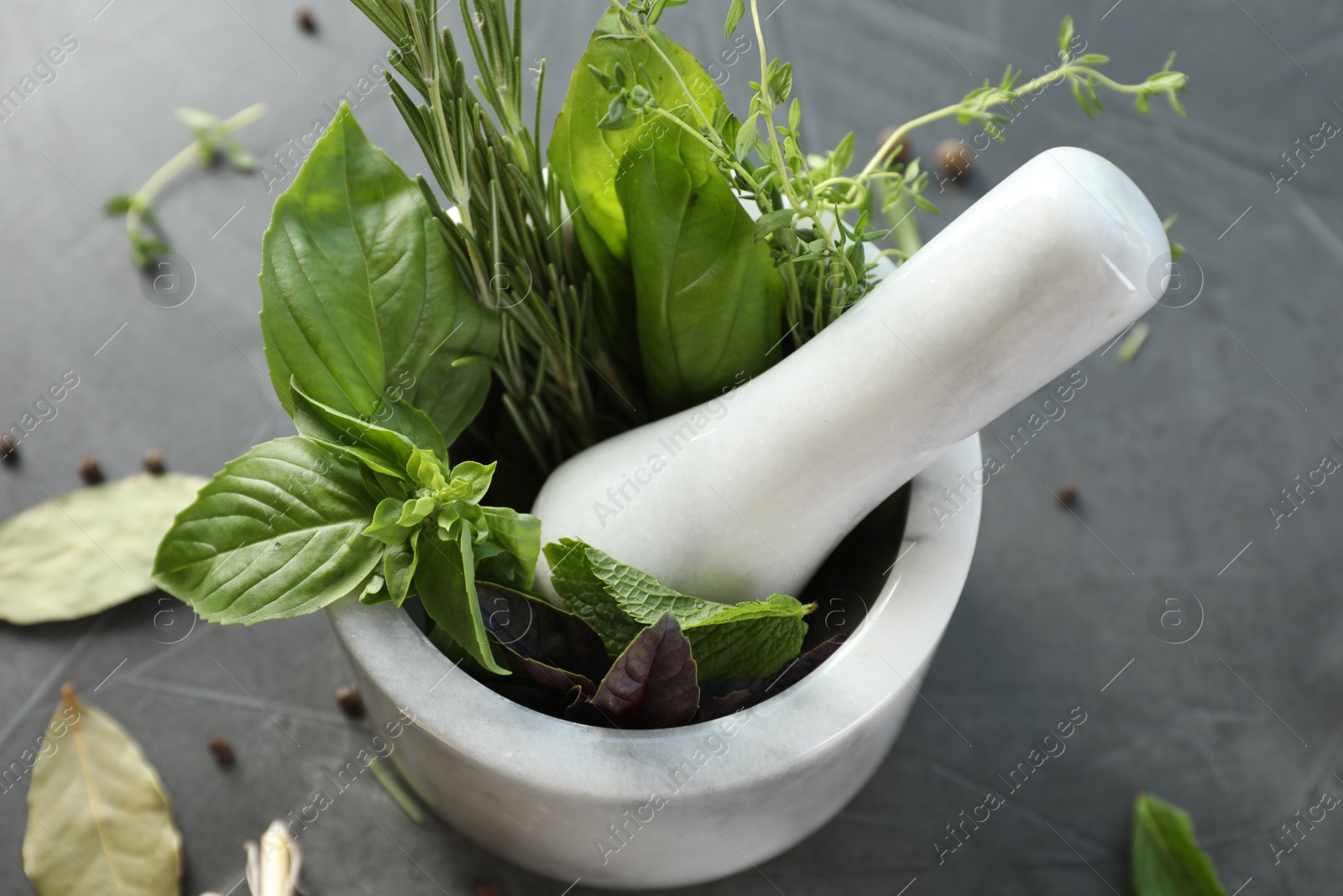 Photo of Different aromatic herbs, mortar with pestle and spices on gray table, closeup