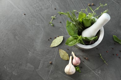 Different aromatic herbs, mortar with pestle and spices on gray textured table, flat lay. Space for text