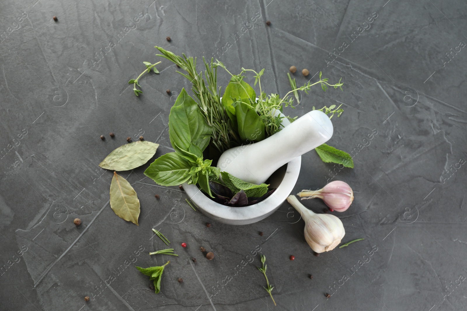 Photo of Different aromatic herbs, mortar with pestle and spices on gray textured table, flat lay