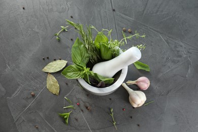 Photo of Different aromatic herbs, mortar with pestle and spices on gray textured table, flat lay