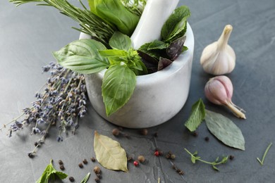 Photo of Different aromatic herbs, mortar with pestle and spices on gray textured table, closeup