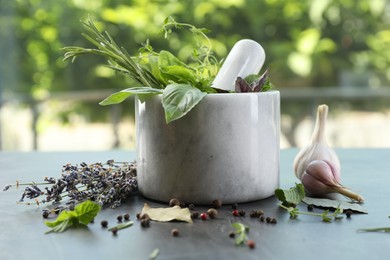 Photo of Different aromatic herbs, mortar with pestle and spices on gray table