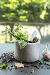 Photo of Different aromatic herbs, mortar with pestle and spices on gray table