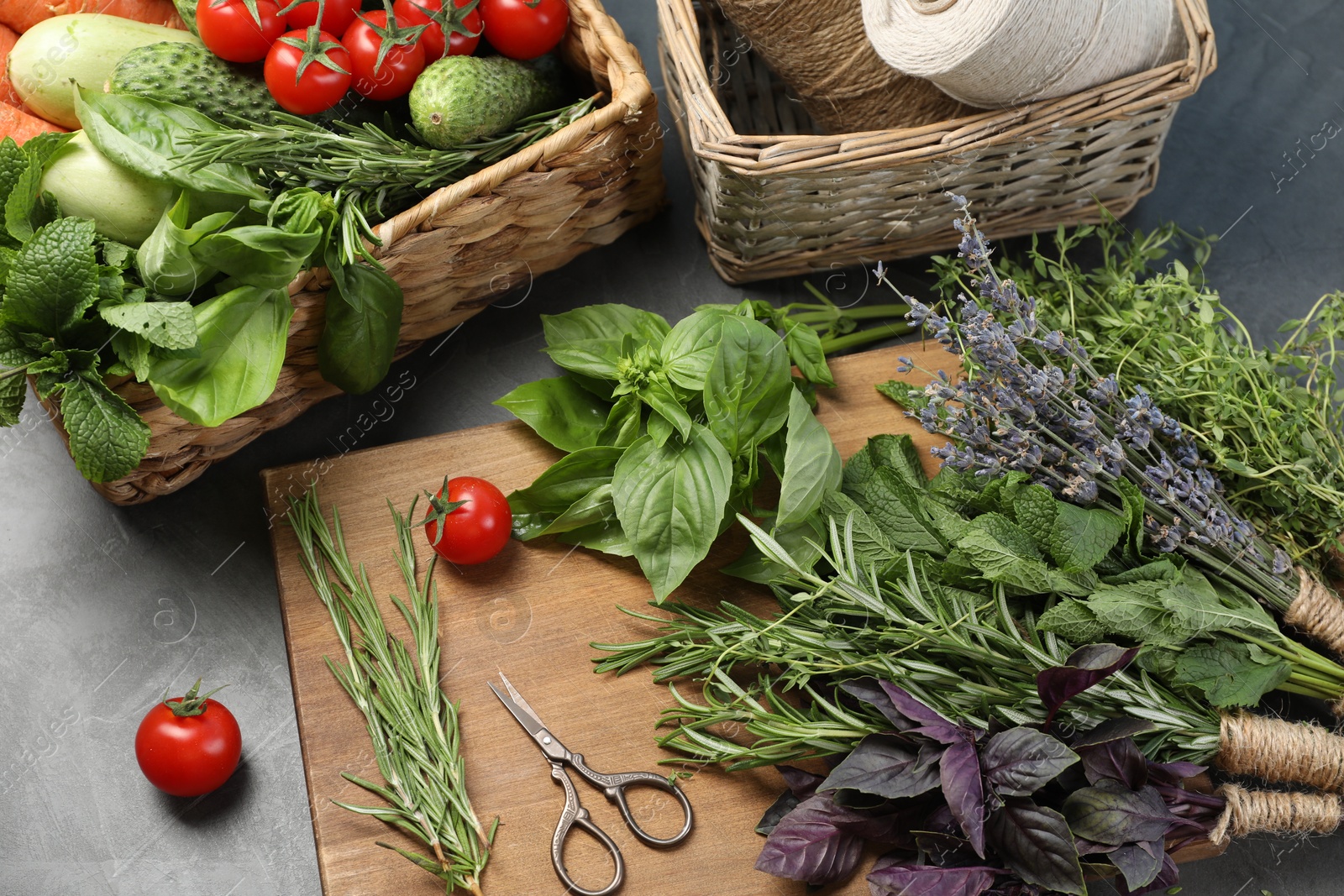 Photo of Different aromatic herbs, vegetables, scissors and threads on gray table, closeup