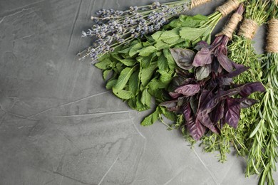 Bunches of different aromatic herbs on gray textured table, top view. Space for text