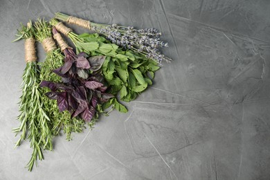 Photo of Bunches of different aromatic herbs on gray textured table, top view. Space for text