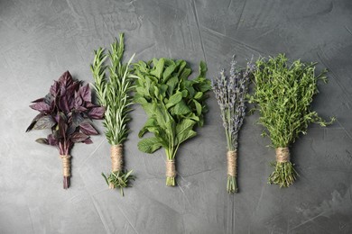 Photo of Bunches of different aromatic herbs on gray textured table, flat lay