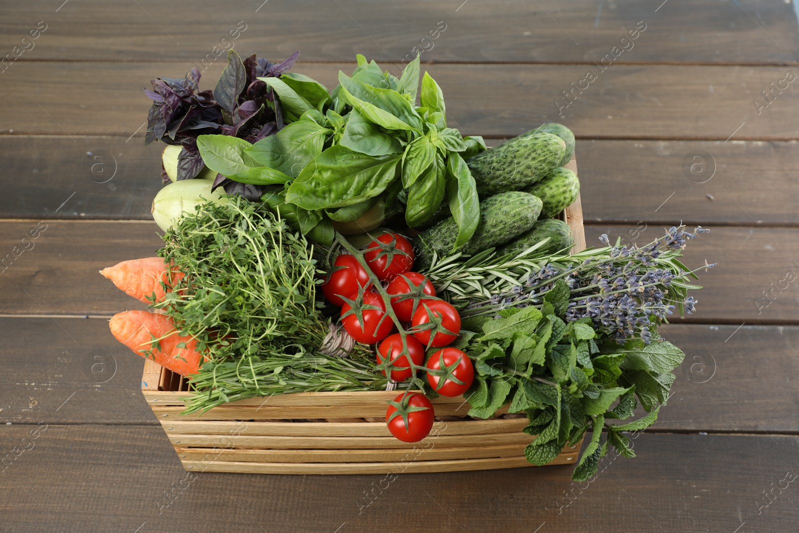 Photo of Different aromatic herbs and vegetables in crate on wooden table, above view