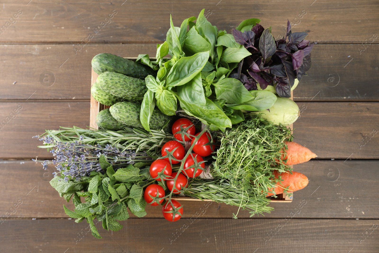 Photo of Different aromatic herbs and vegetables in crate on wooden table, top view