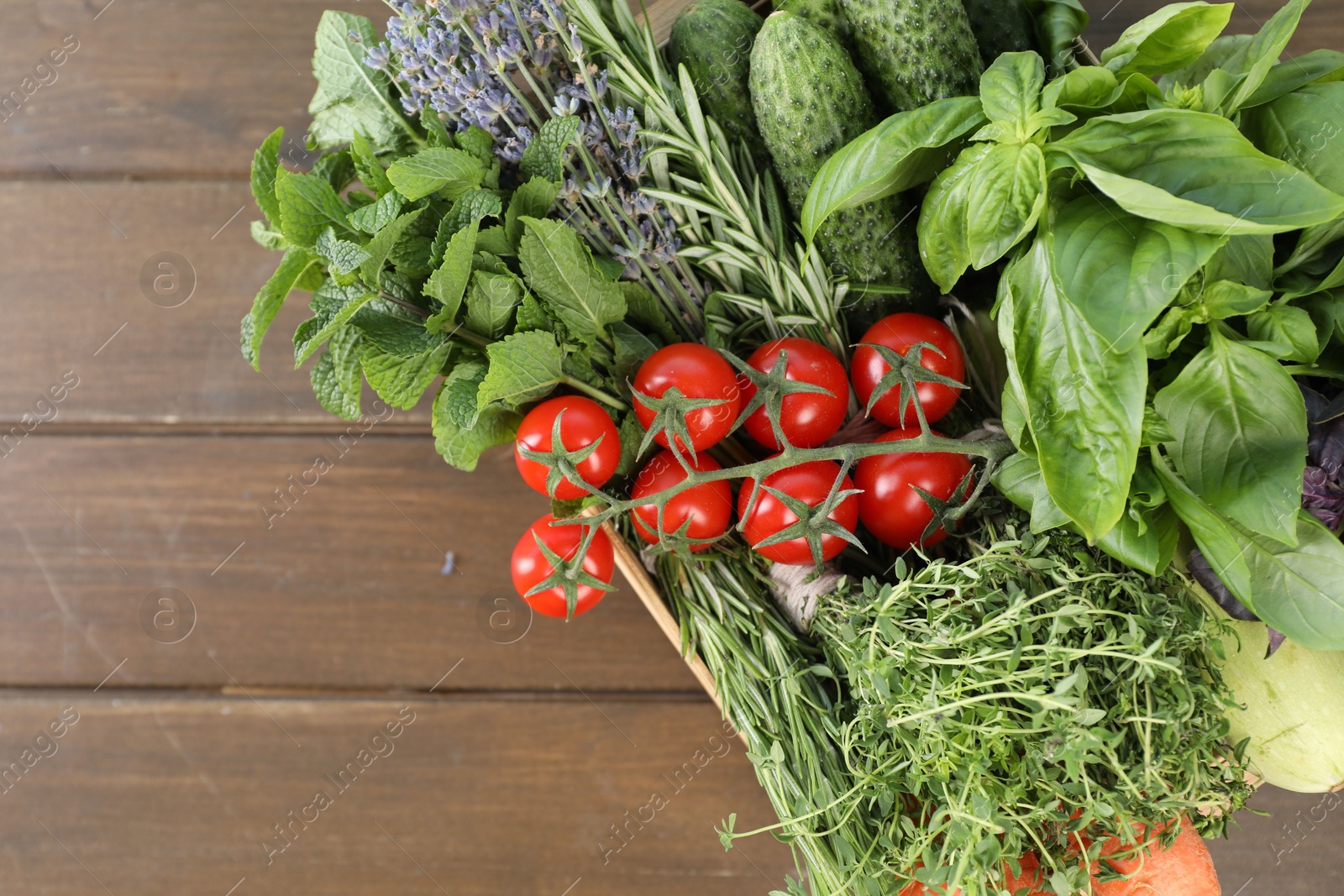 Photo of Different aromatic herbs and vegetables in crate on wooden table, top view. Space for text