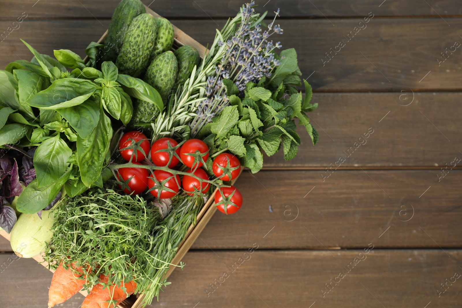 Photo of Different aromatic herbs and vegetables in crate on wooden table, top view. Space for text