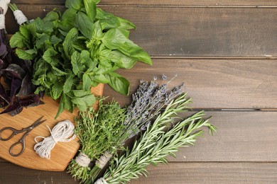 Photo of Different aromatic herbs, thread and scissors on wooden table, top view. Space for text