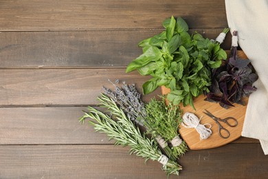 Photo of Different aromatic herbs, thread and scissors on wooden table, top view. Space for text