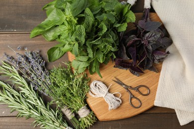 Photo of Different aromatic herbs, thread and scissors on wooden table, top view