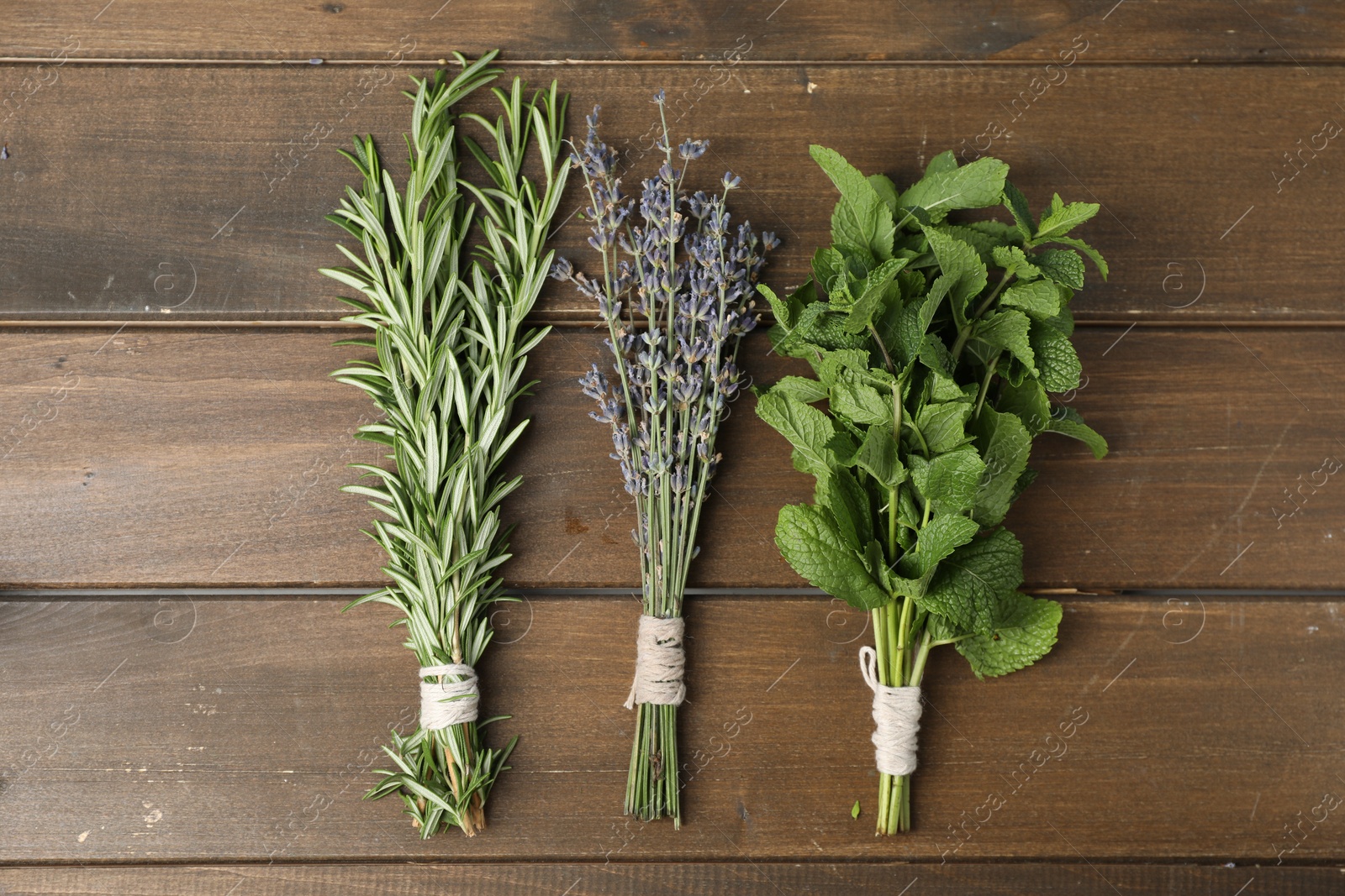 Photo of Bunches of different aromatic herbs on wooden table, flat lay