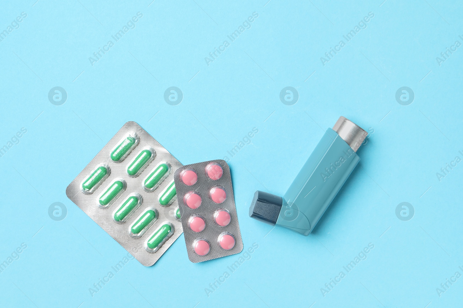 Photo of Asthma inhaler and pills on light blue background, flat lay