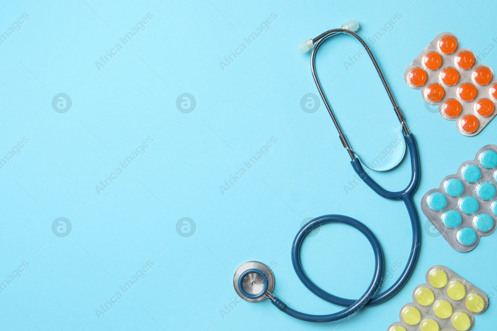 Photo of Stethoscope and pills on light blue background, flat lay. Space for text