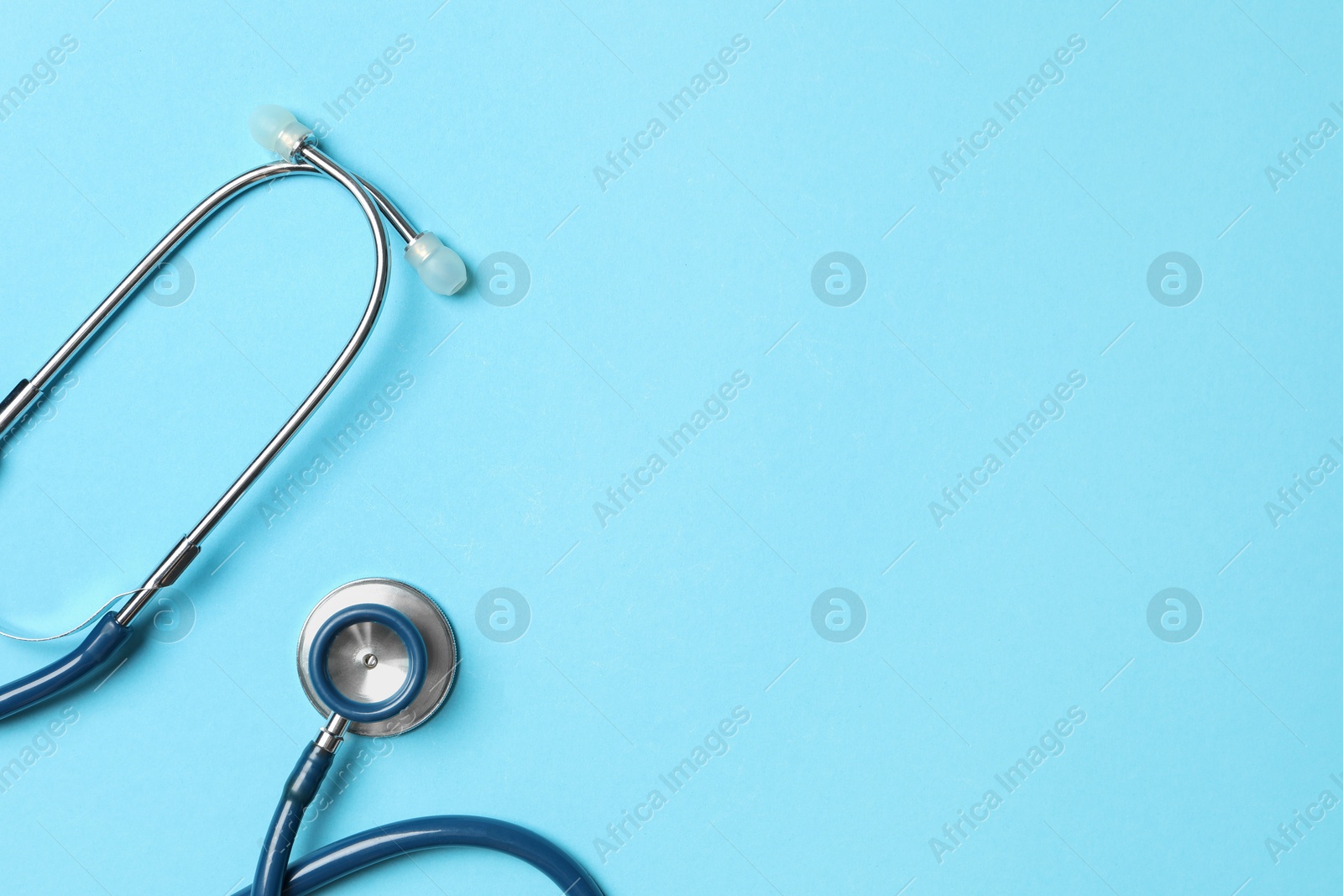 Photo of Stethoscope on light blue background, top view. Space for text