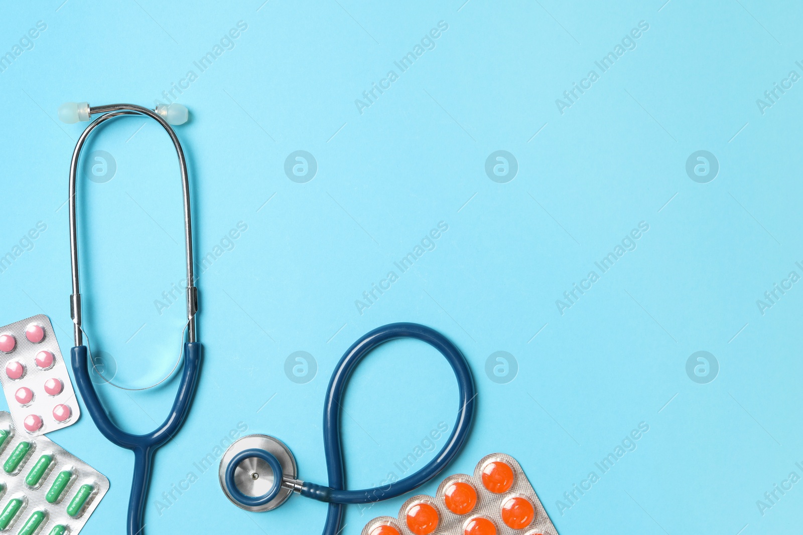 Photo of Stethoscope and pills on light blue background, flat lay. Space for text