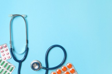 Photo of Stethoscope and pills on light blue background, flat lay. Space for text