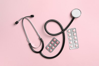 Photo of Stethoscope and pills on pink background, flat lay