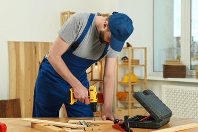 Photo of Craftsman working with drill at wooden table in workshop