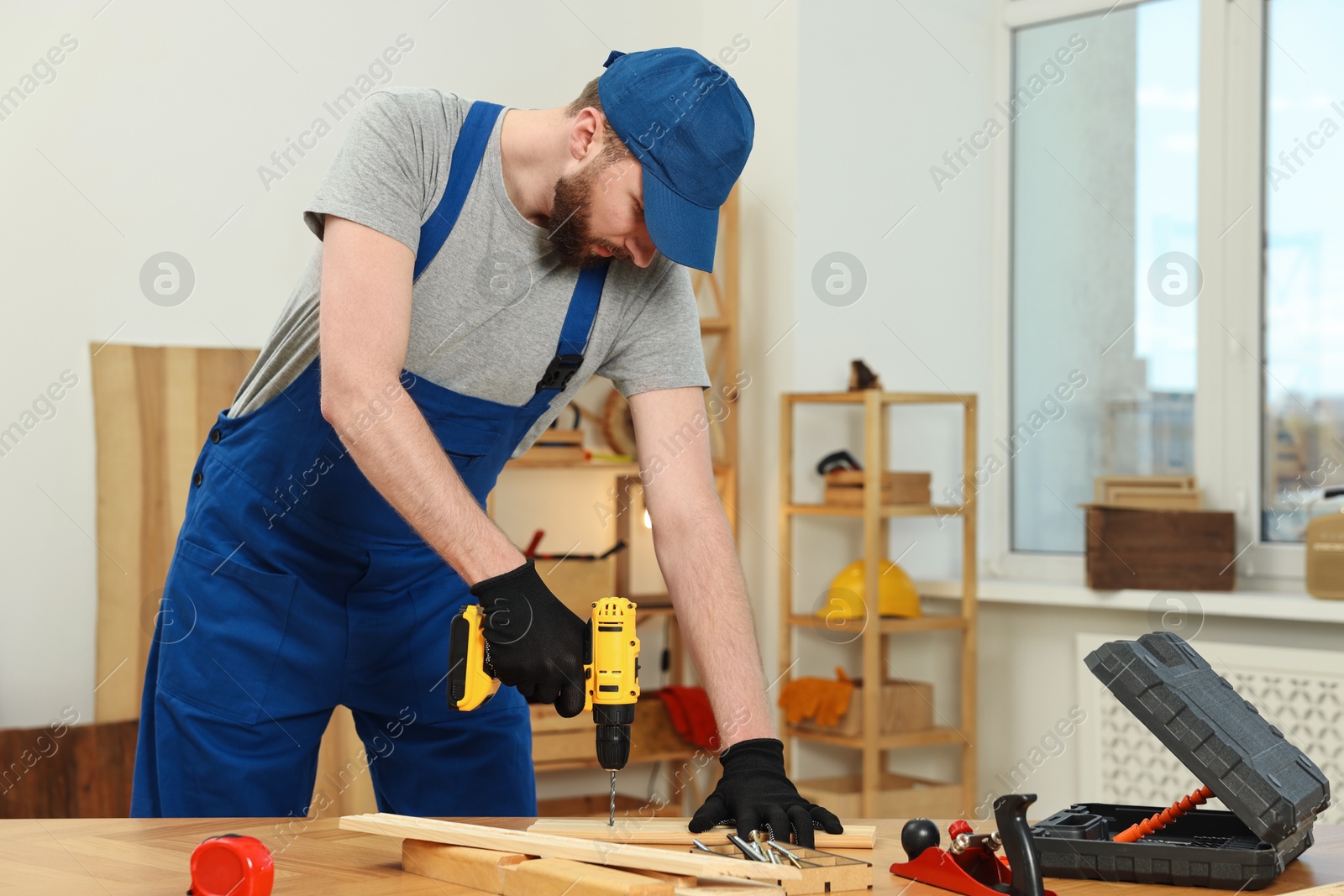 Photo of Craftsman working with drill at wooden table in workshop