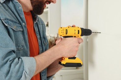 Photo of Smiling man drilling white wall at home, closeup