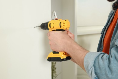 Photo of Man drilling white wall at home, closeup