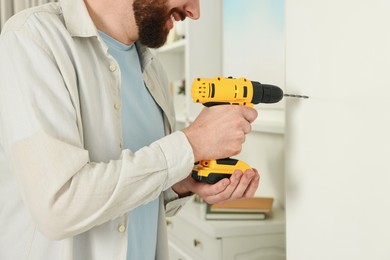Photo of Smiling man drilling white wall at home, closeup