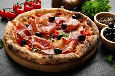 Photo of Tasty pizza with cured ham, olives, tomatoes, parsley and spices on black table