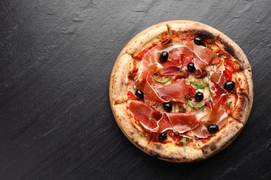 Photo of Tasty pizza with cured ham, olives and sun-dried tomato on black table, top view. Space for text